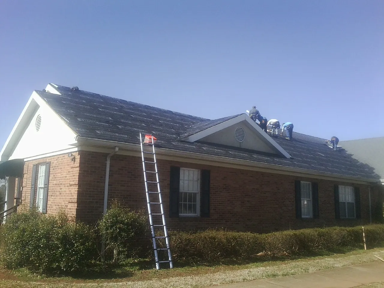 Crew tearing shingles off a brick ranch roof with a ladder set — Metal Roof Repair work by our crew in Sparrow Bush
