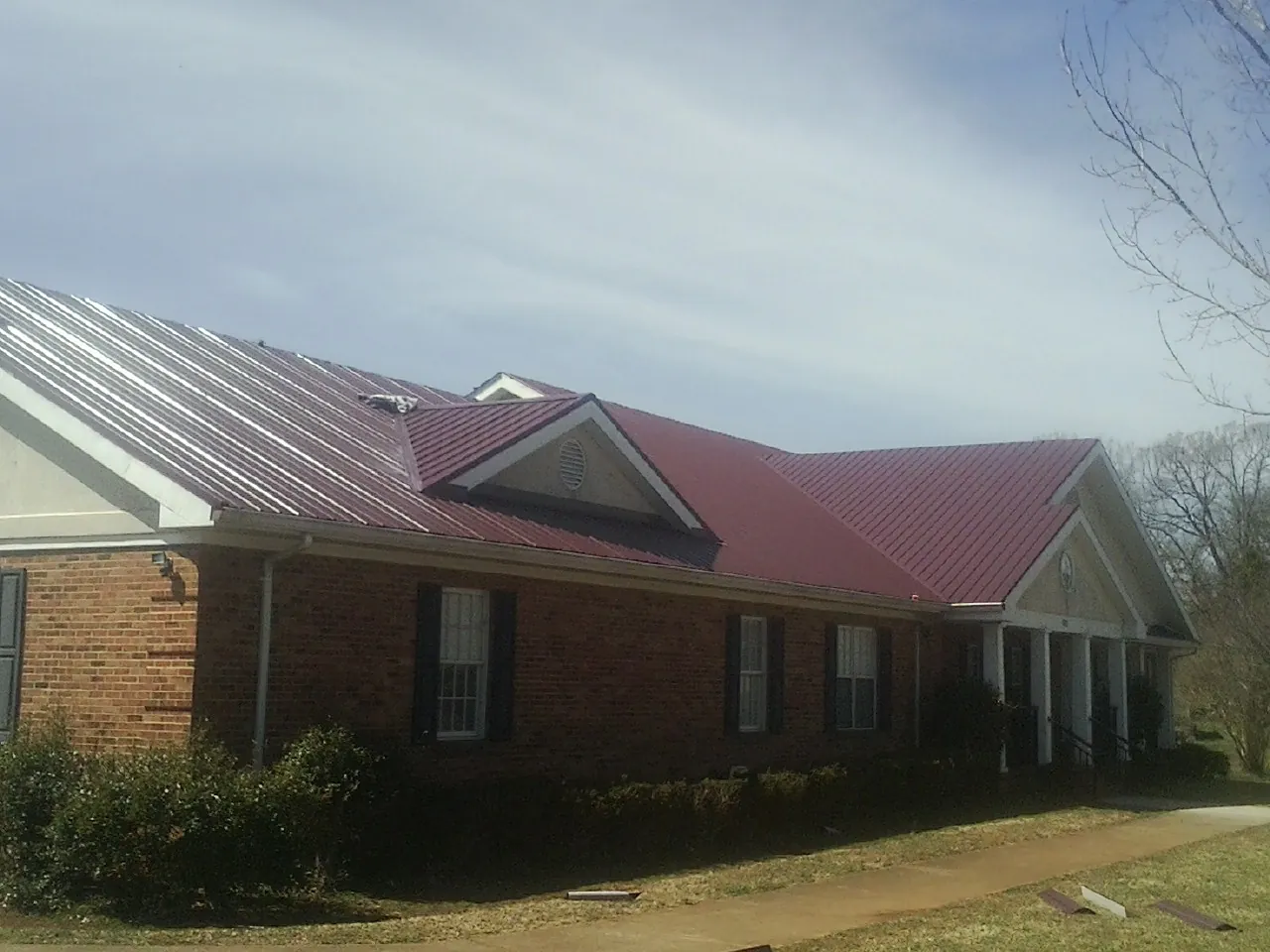 Red metal roof with gabled entries on a long brick building, from a Hail Damage Roof Repair job in Sparrow Bush