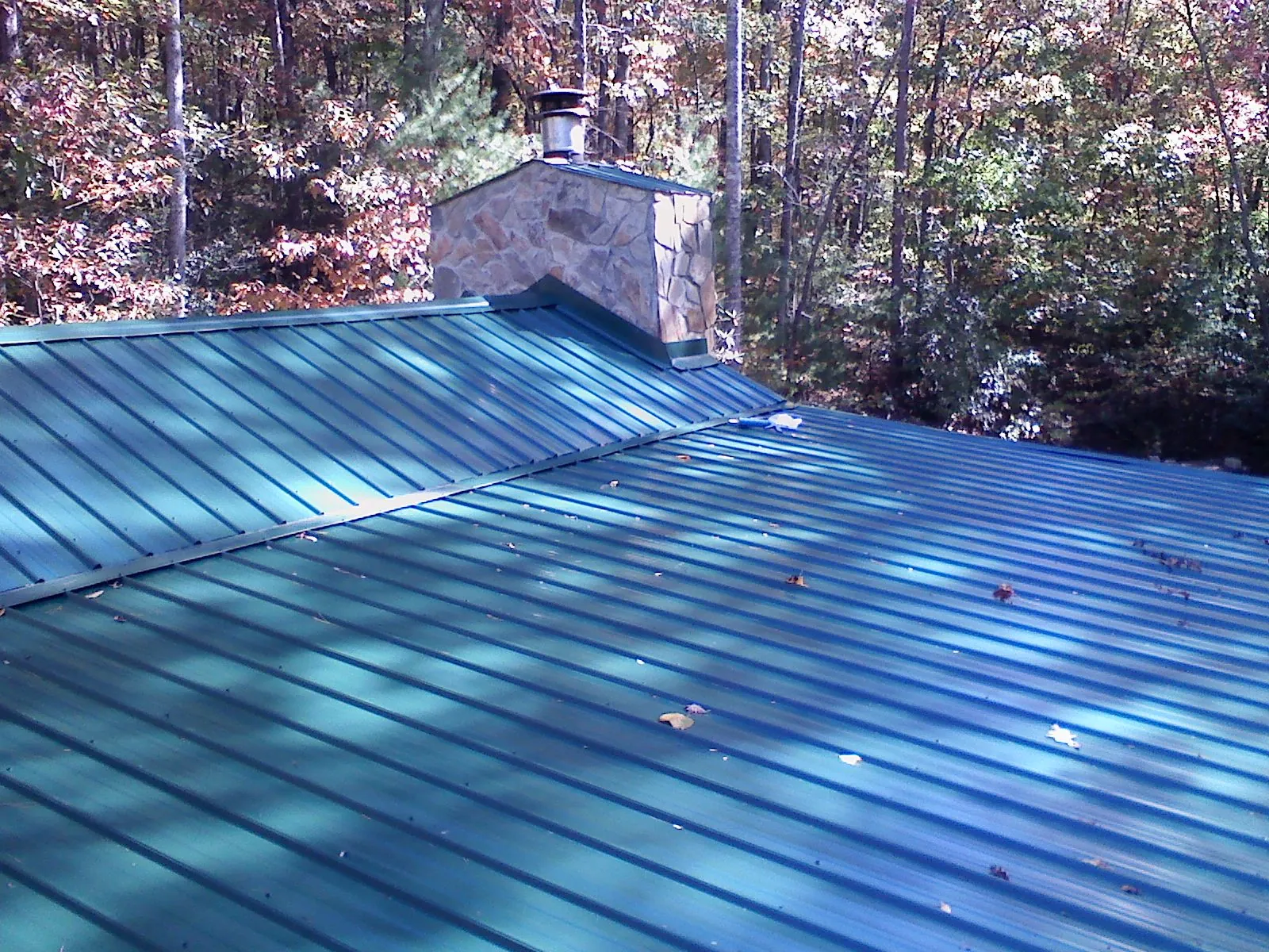 New green metal roof and stone chimney surrounded by autumn woods in Sparrow Bush