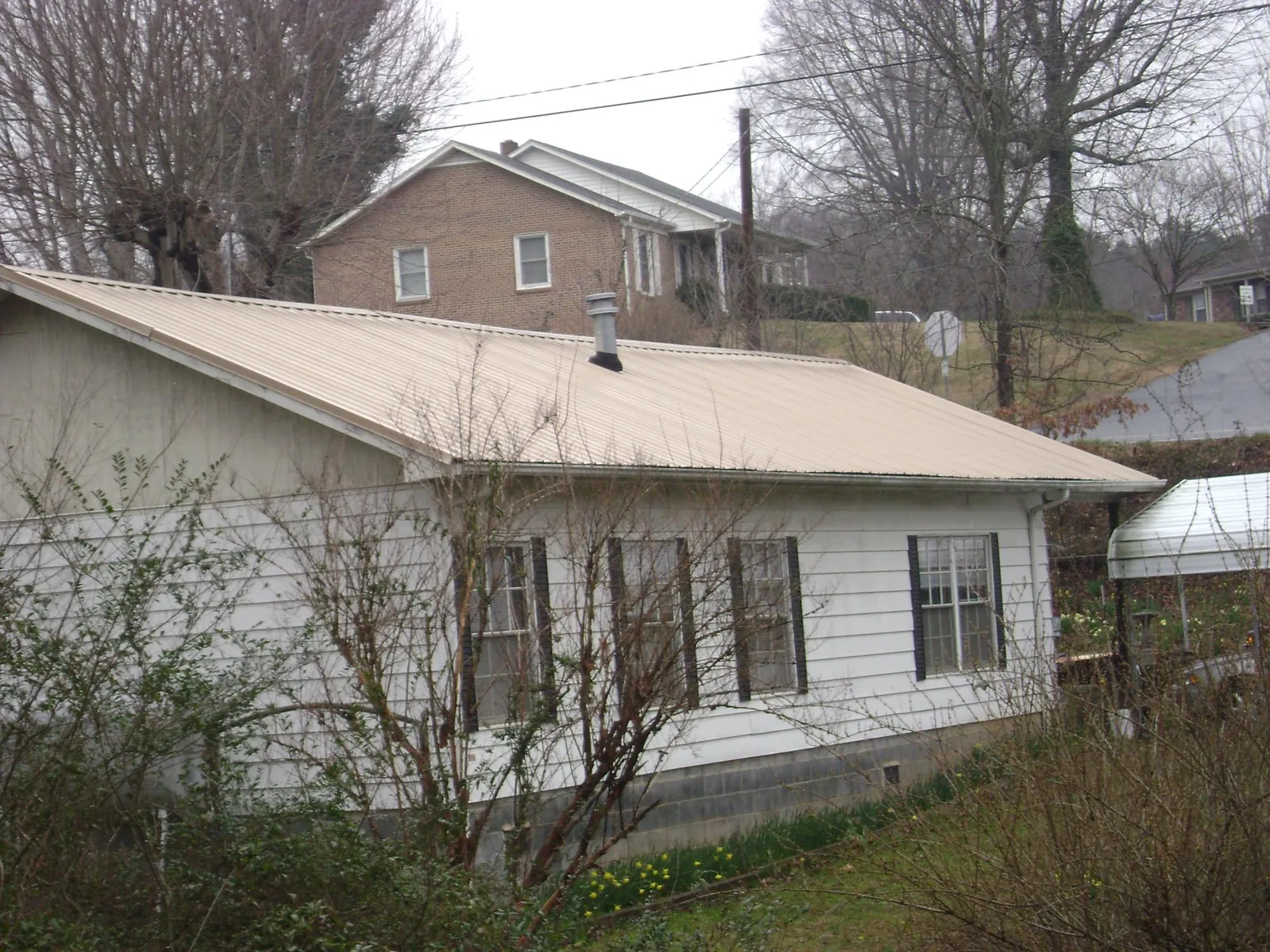 Tan metal roof on a white sided house set into a hillside — Commercial Roofing by Roofing Brothers in Sparrow Bush